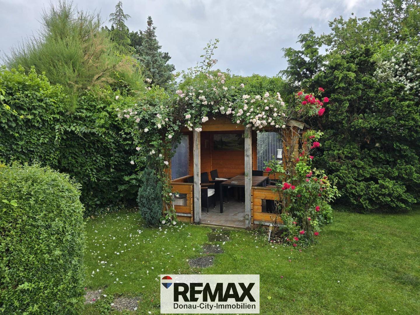 Charmantes Holzpavillon im Garten, umgeben von blühenden Rosen und grünen Pflanzen.