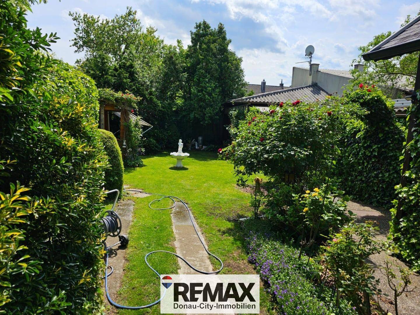 Großer, gepflegter Garten mit Rasenfläche, Wegen und einem dekorativen Brunnen.