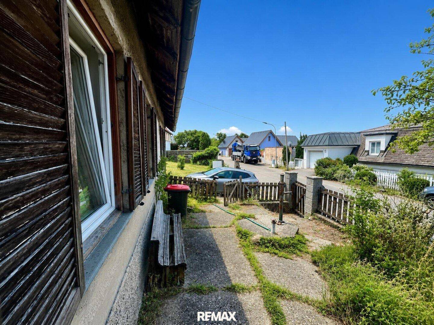 Seitenansicht eines Hauses mit Fensterläden und Blick auf die ländliche Straße und Nachbarschaft.