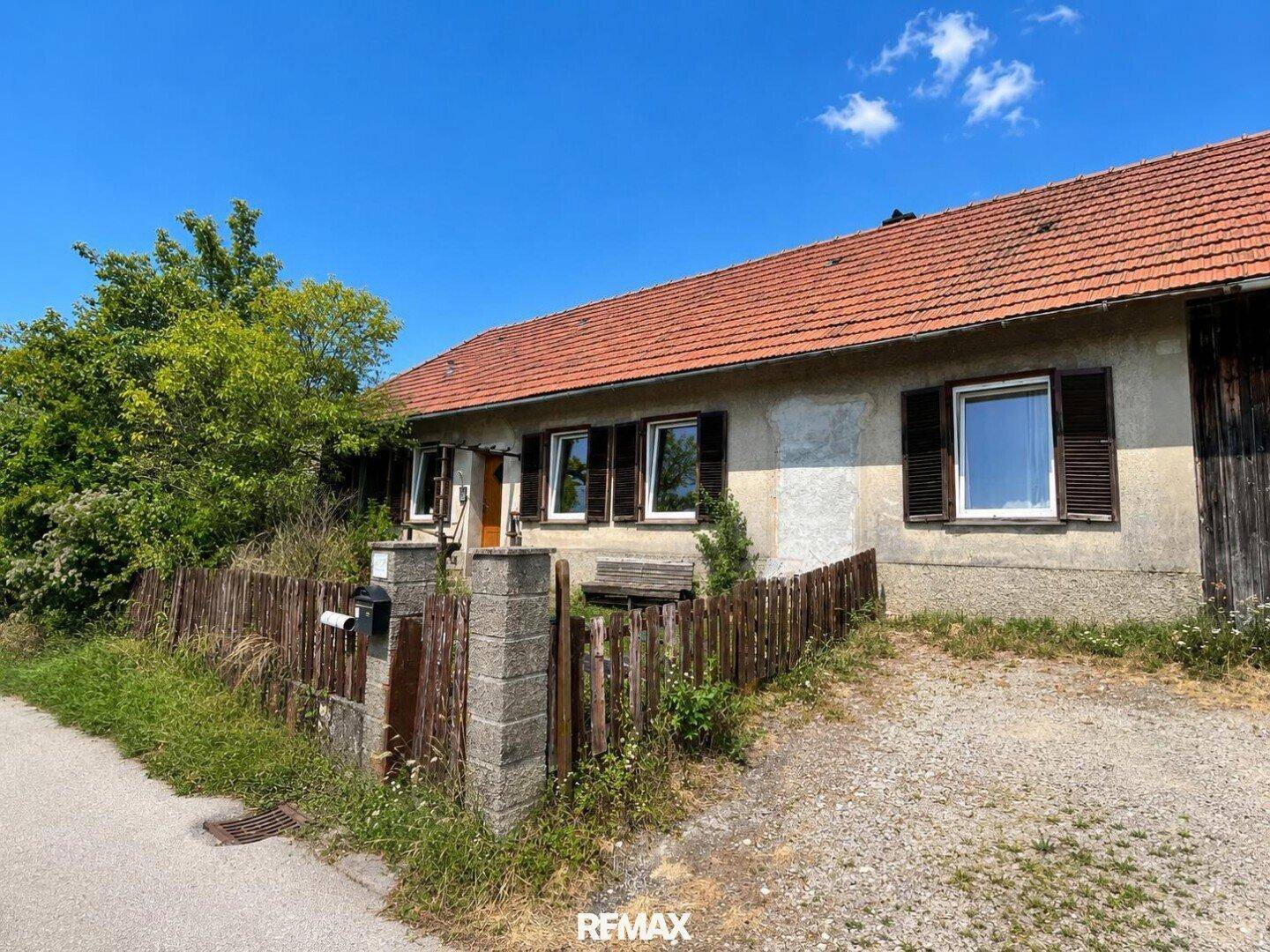 Fassade eines älteren Hauses mit braunen Fensterläden und einem Holzzaun im ländlichen Stil.