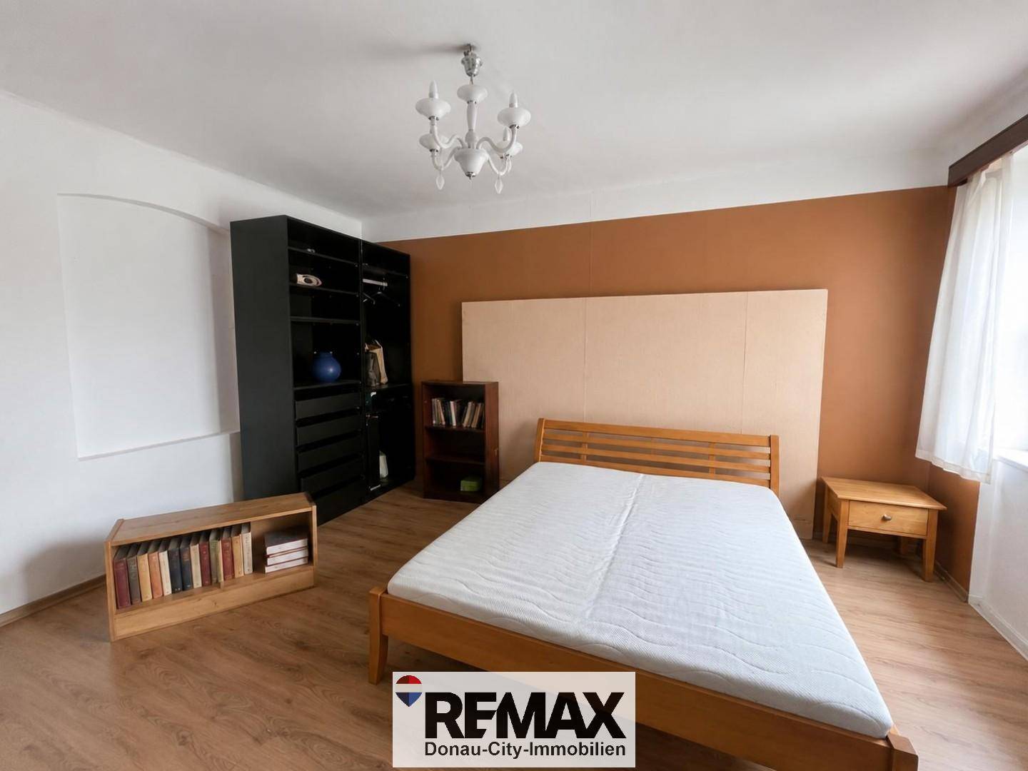 Schlafzimmer mit Holzbett, offenem Kleiderschrank und einer Akzentwand in Erdtönen.