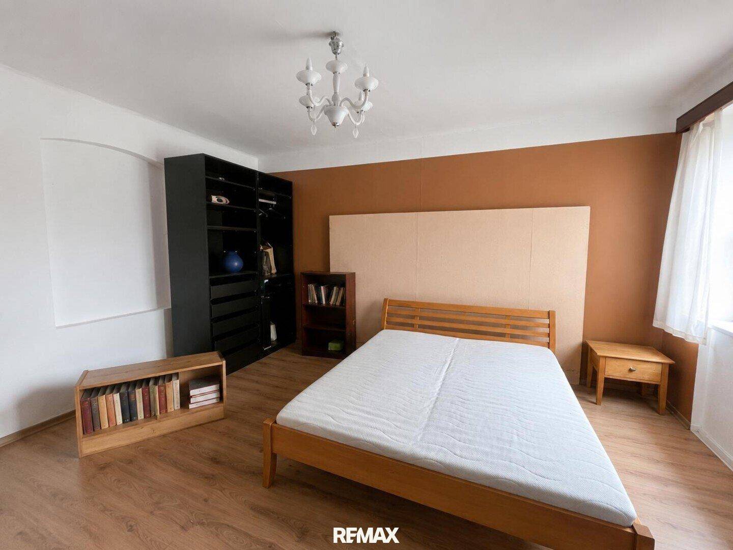 Schlafzimmer mit Holzbett, brauner Akzentwand und einem dunklen Kleiderschrank.