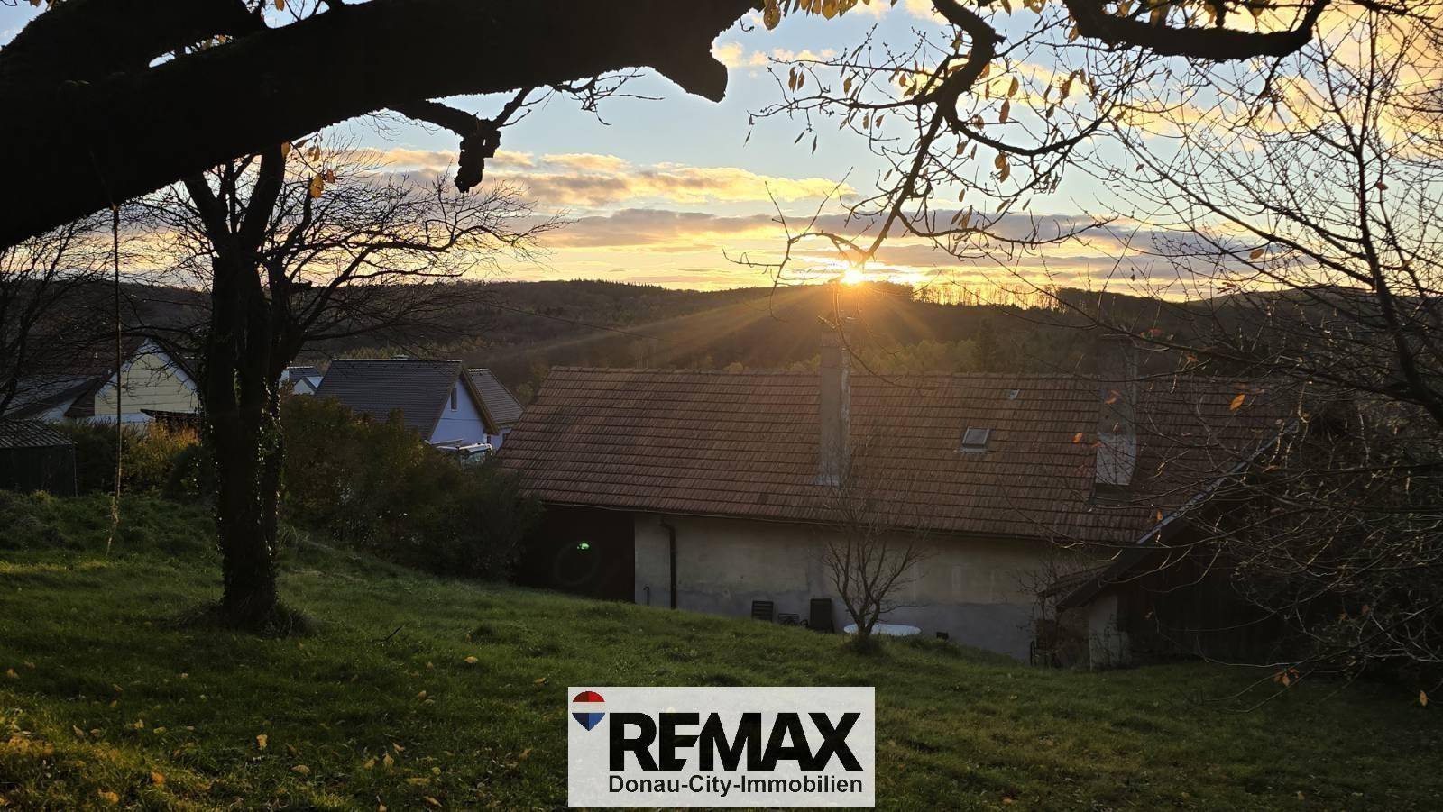 Haus und Garten im warmen Licht des Sonnenuntergangs, umgeben von winterlicher Landschaft.