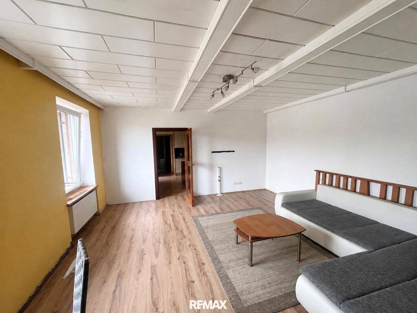 Helles Wohnzimmer mit Laminatboden, weiß gestrichenen Wänden und einem modernen Sofa.