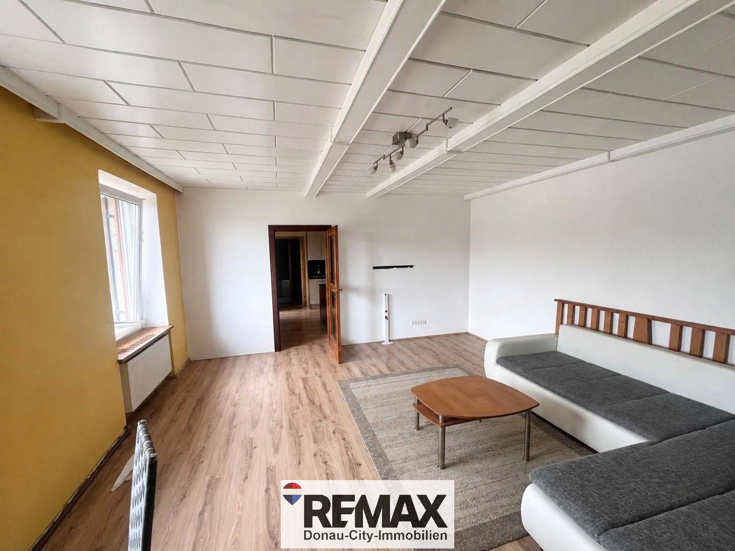 Geräumiges Wohnzimmer mit Laminatboden, weiß gestrichenen Wänden und einer modernen Couch.