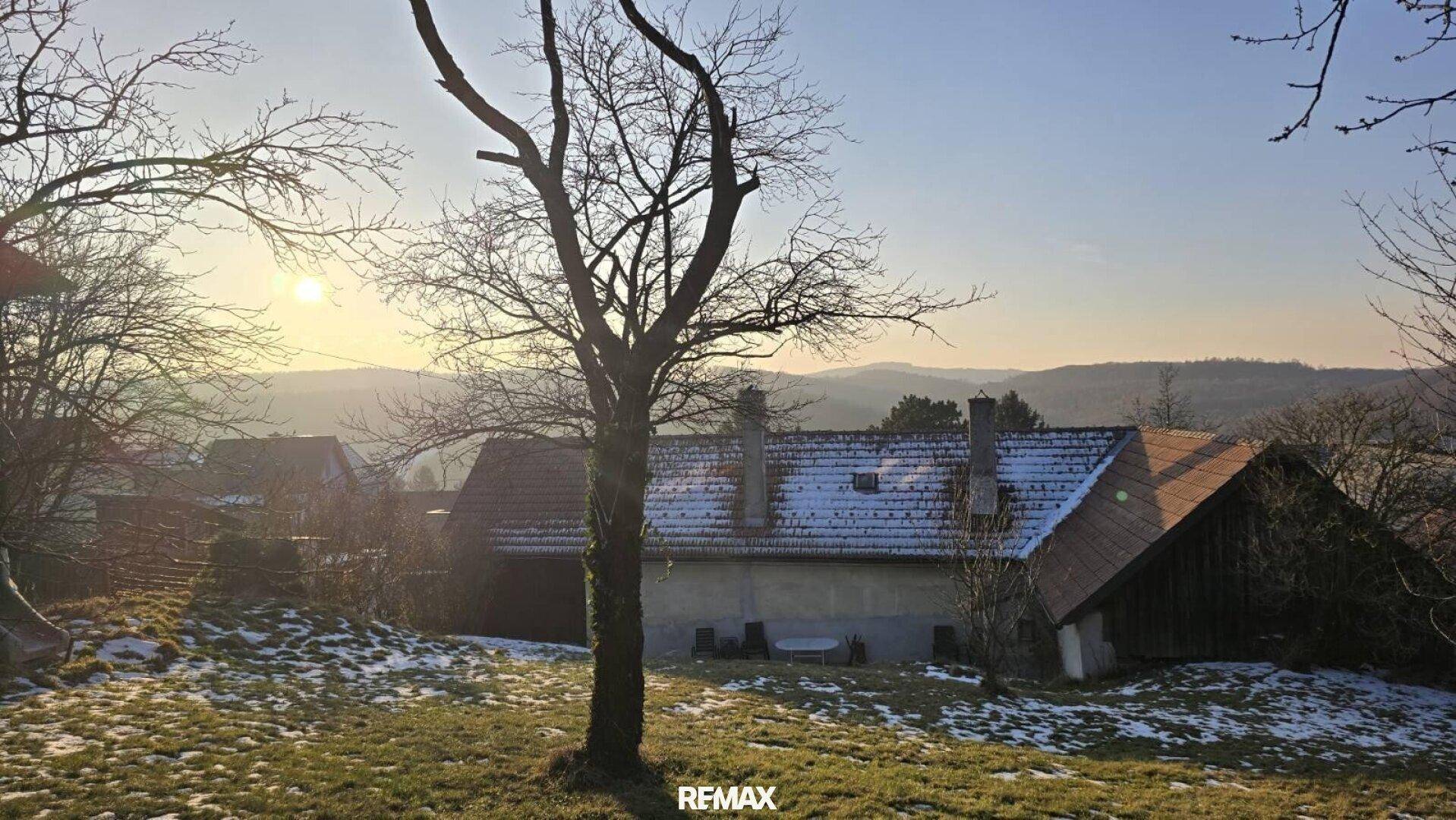 Winterlandschaft bei Sonnenuntergang mit schneebedeckten Dächern und kahlen Bäumen.