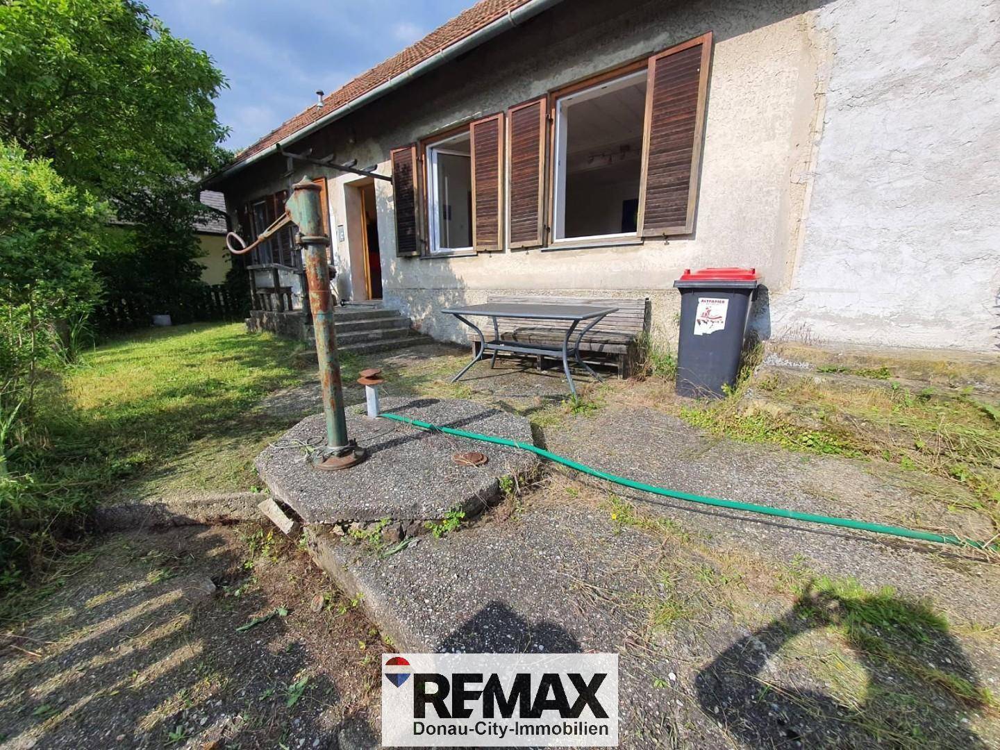 Kleiner gepflasterter Bereich neben dem Haus mit einem alten Wasserbrunnen und Sitzgelegenheit.
