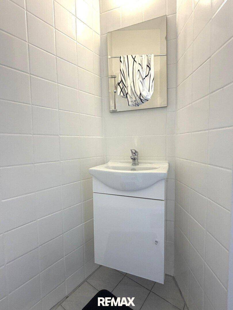 Kleines Badezimmer mit weißen Fliesen, modernem Waschbecken und Spiegel.