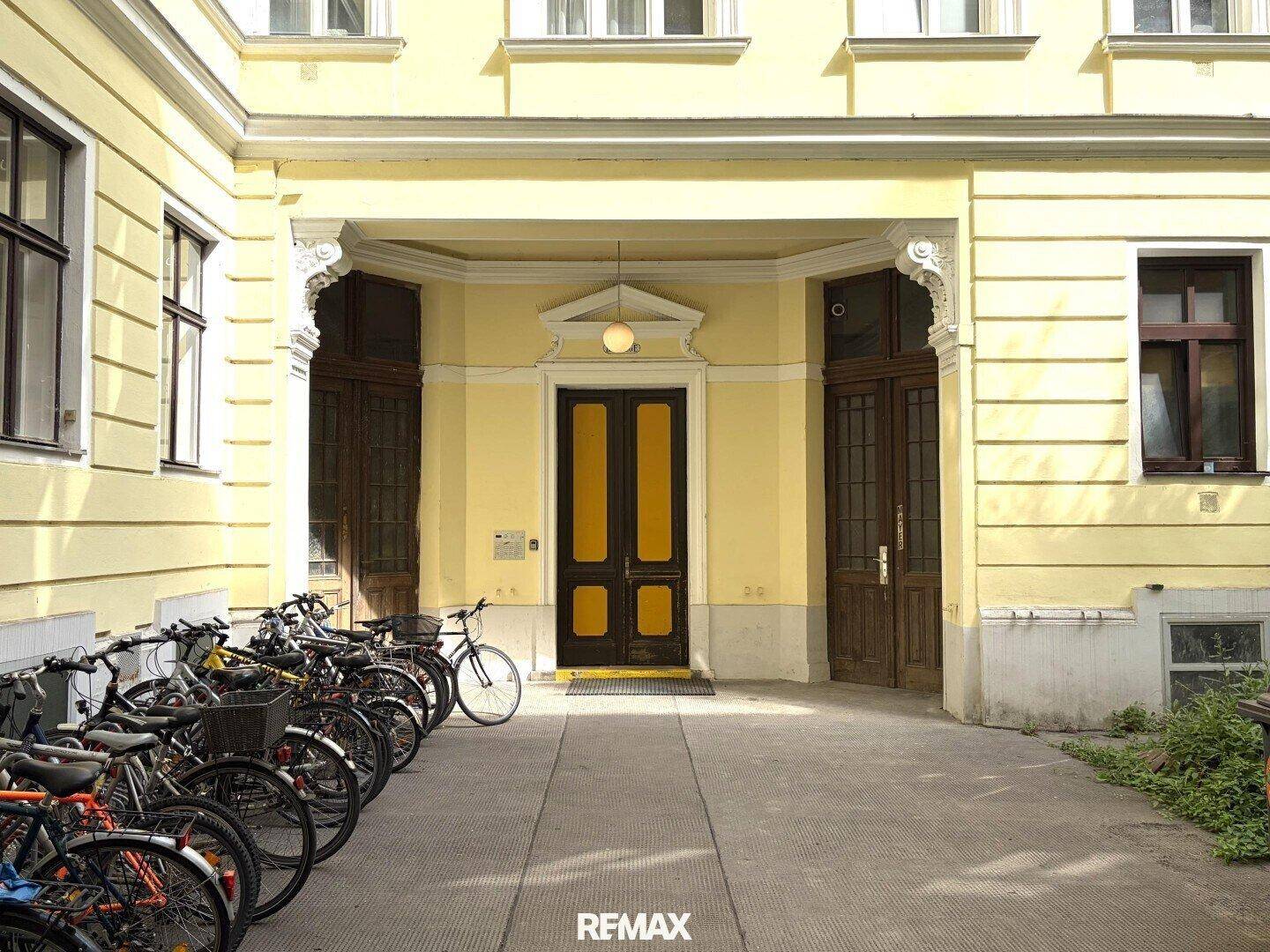 Historische Fassade eines Gebäudes mit gelbem Anstrich und Fahrradabstellplätzen im Hof.
