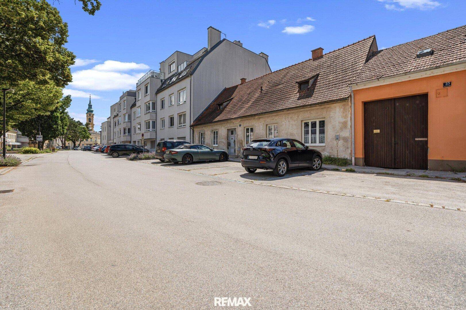 Straßenansicht mit einem traditionellen Haus und einem modernen Mehrfamilienhaus im Hintergrund.