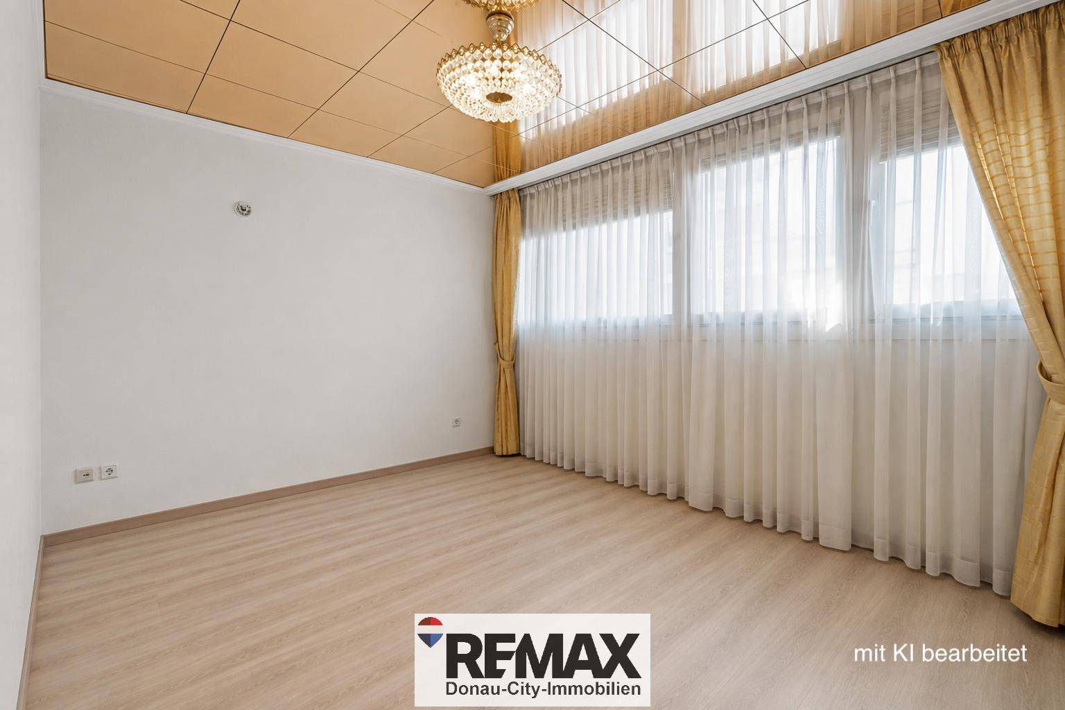 Heller Raum mit Laminatboden, großen Fenstern und einem dekorativen Kronleuchter an der Decke.