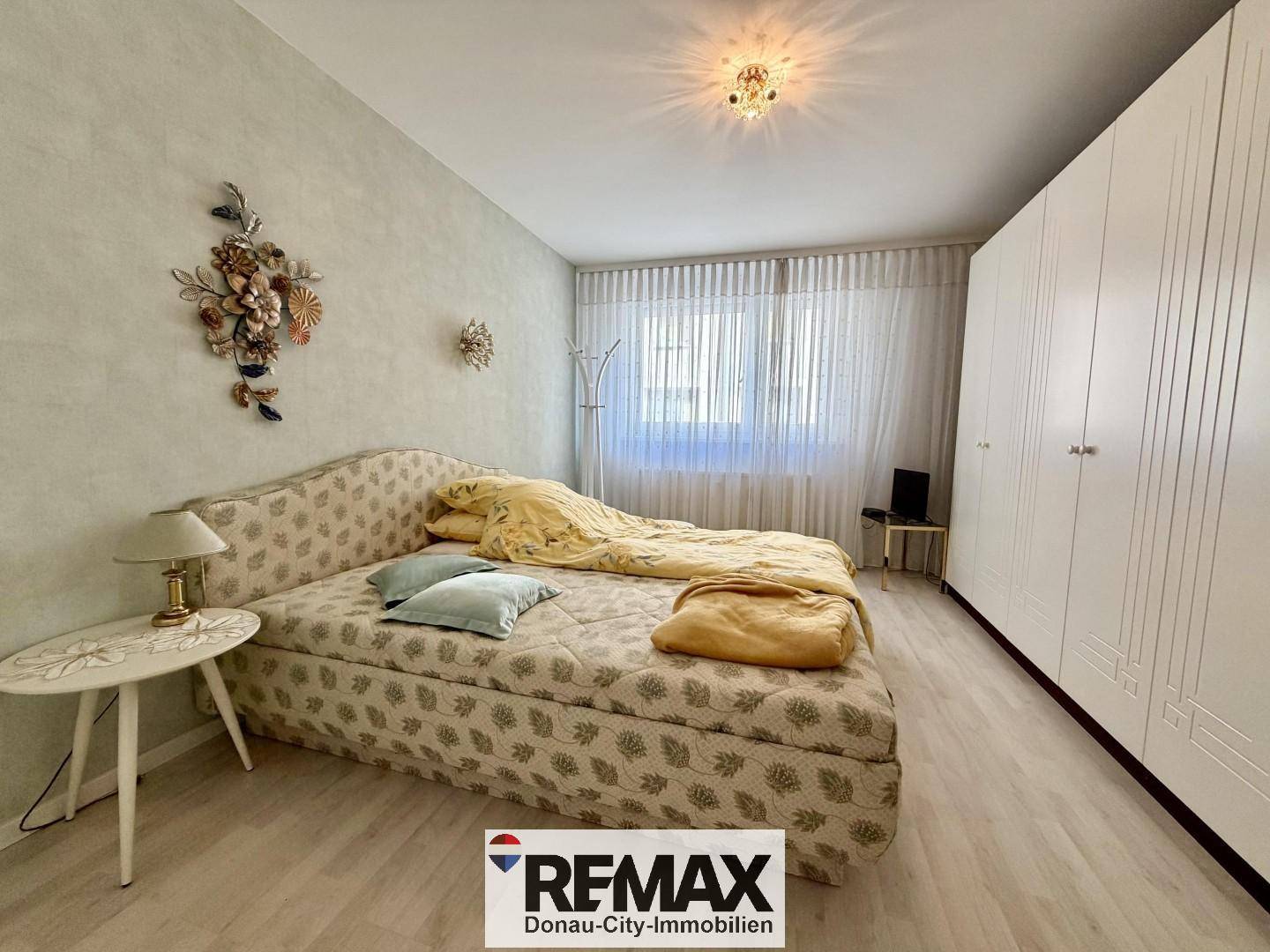 Schlafzimmer mit Bett, großem weißen Kleiderschrank und hellem Laminatboden.