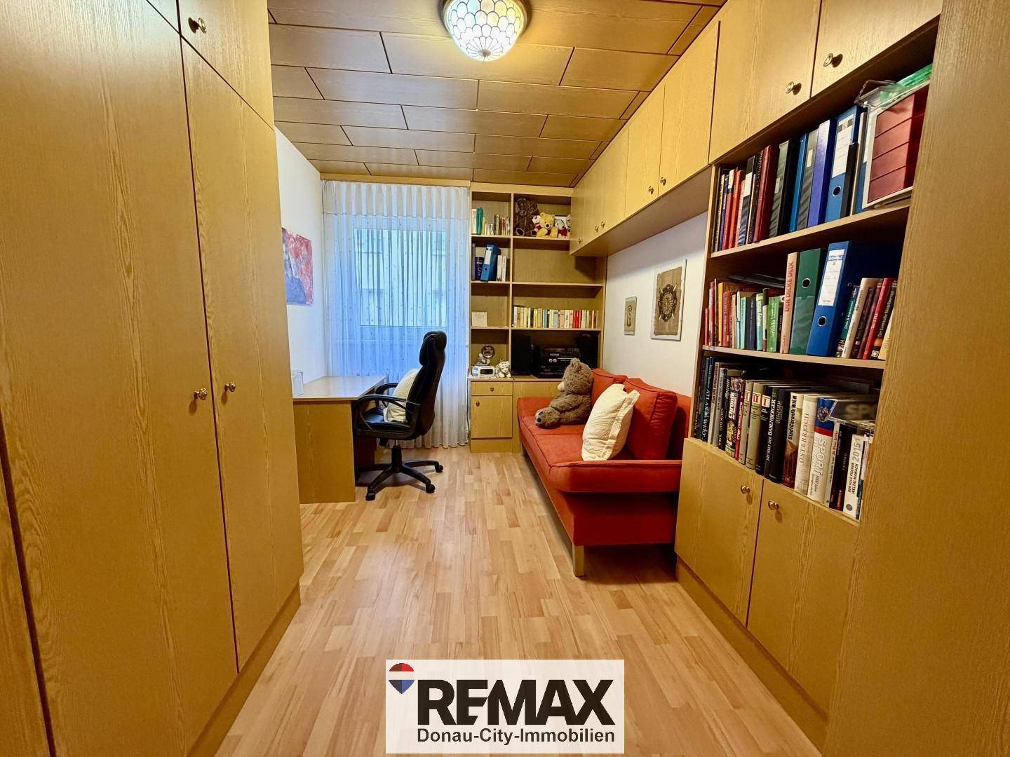 Arbeitszimmer mit Schreibtisch, Bürostuhl und vielen eingebauten Holzschränken.