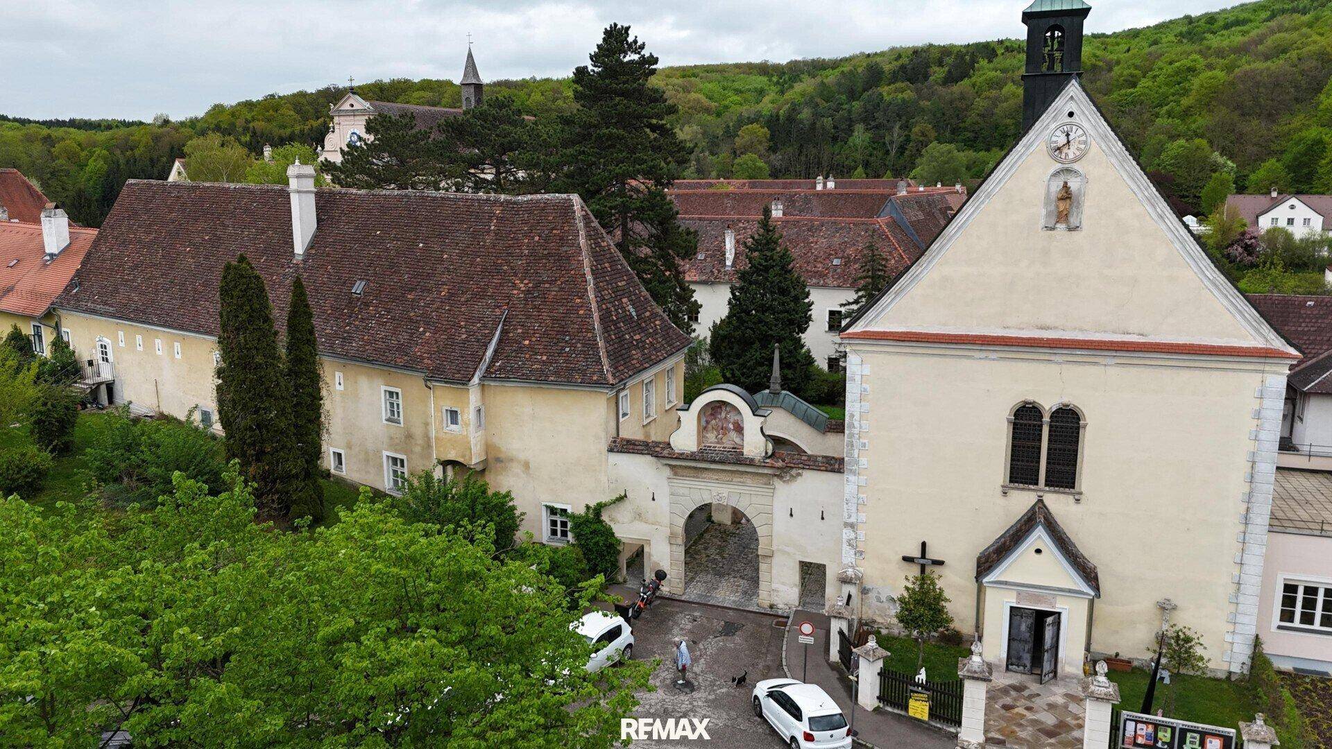 Historische Klosteranlage mit Kirche und umliegenden Gebäuden, eingebettet in grüne Landschaft.