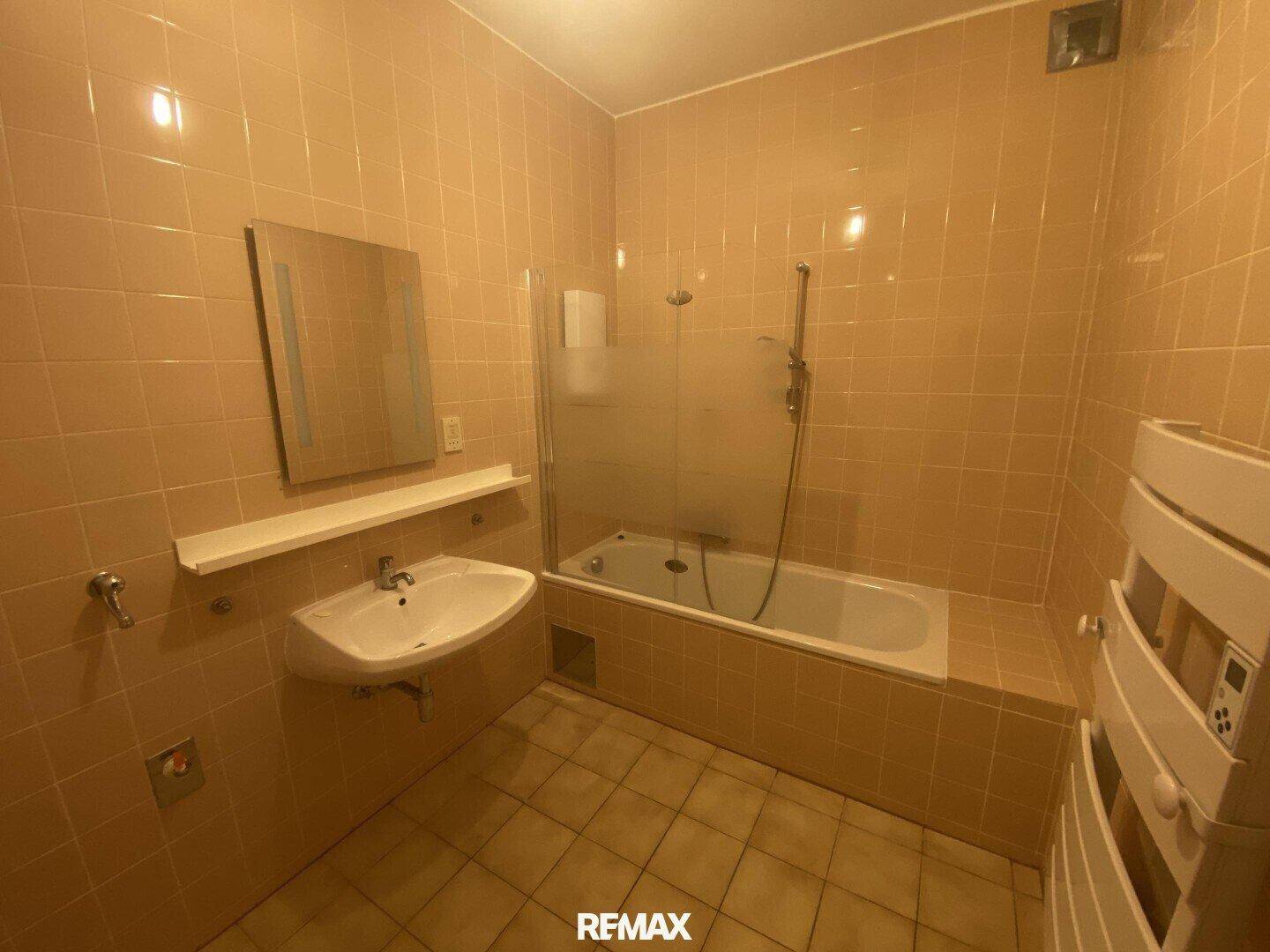 Gefliestes Badezimmer in Beige mit Badewanne, Waschbecken und beheiztem Handtuchhalter.