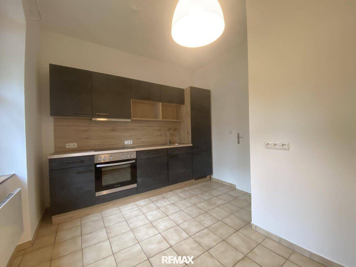 Moderne Einbauküche mit dunklen Schränken, Holzoptik-Arbeitsplatte und Fliesenboden.