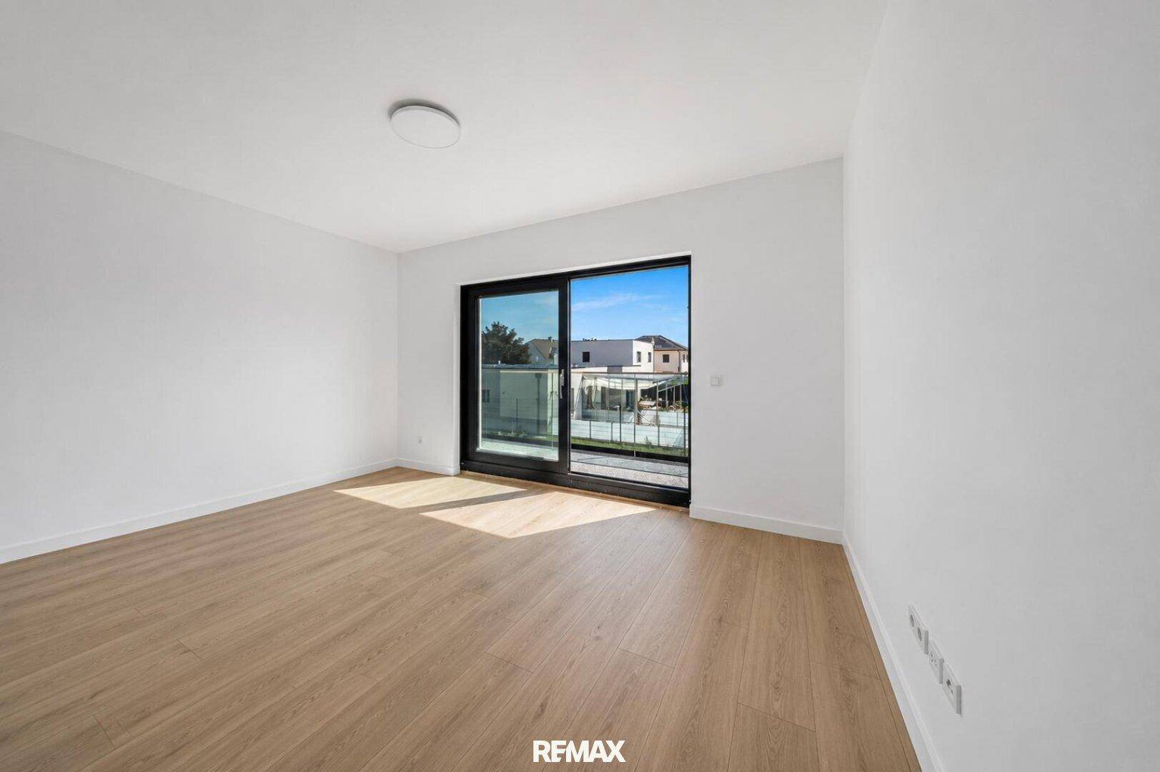Geräumiger, leerer Raum mit Holzboden und Zugang zu einem französischen Balkon.