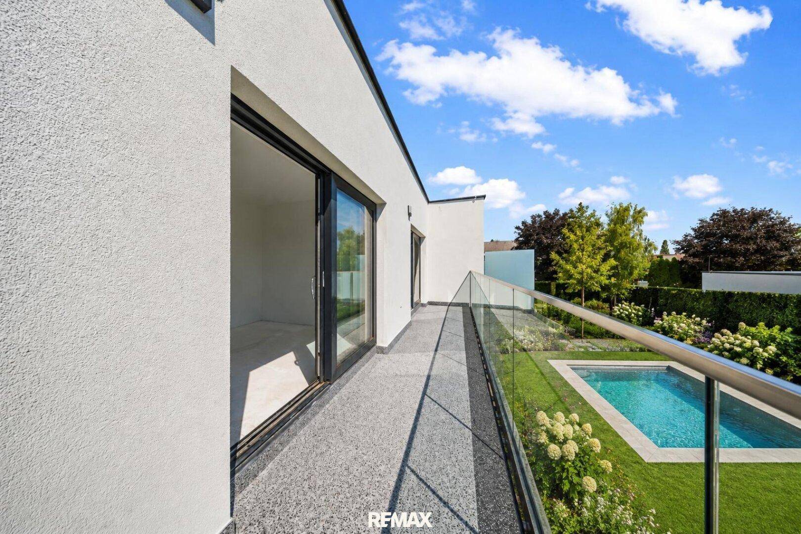Moderner Balkon mit Glasgeländer und Blick auf den Garten mit Pool.