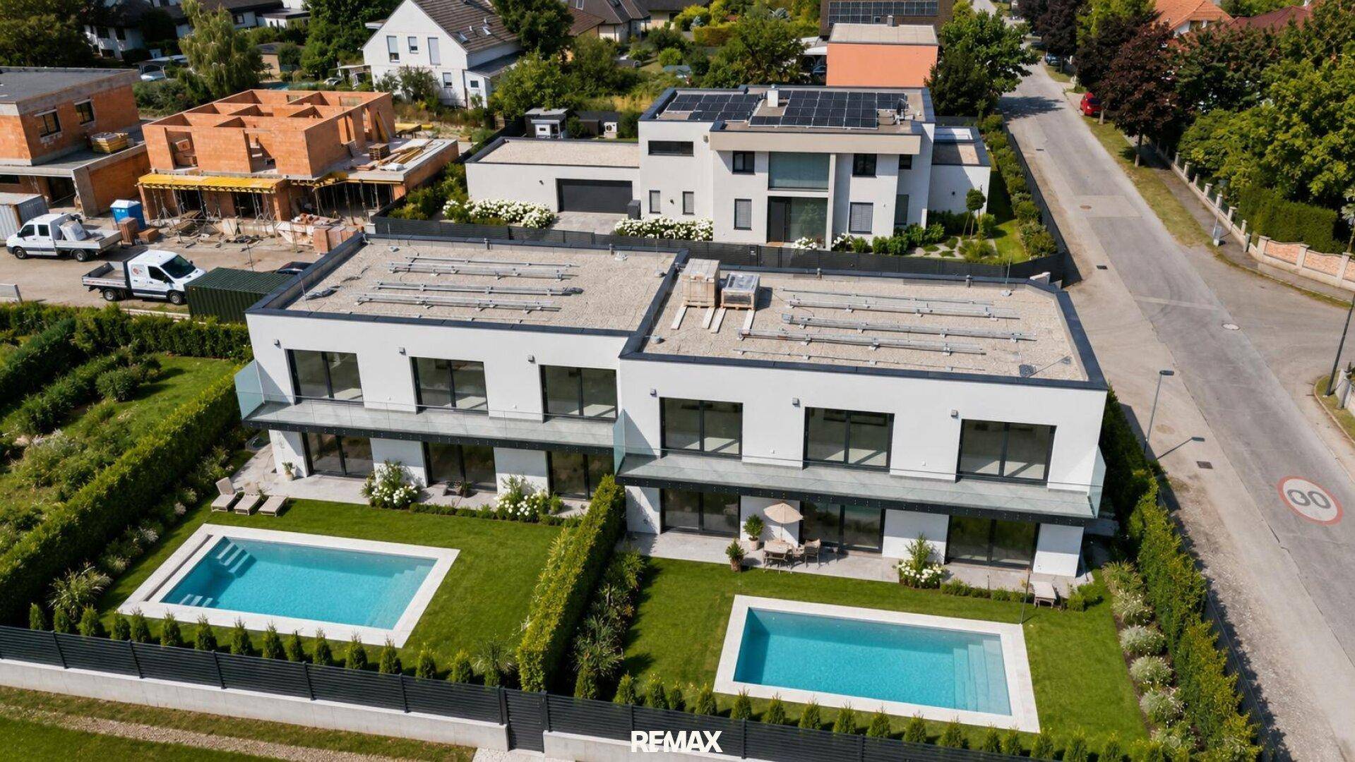 Luftaufnahme von zwei modernen Häusern mit Pools, Solaranlagen und angrenzender Baustelle.