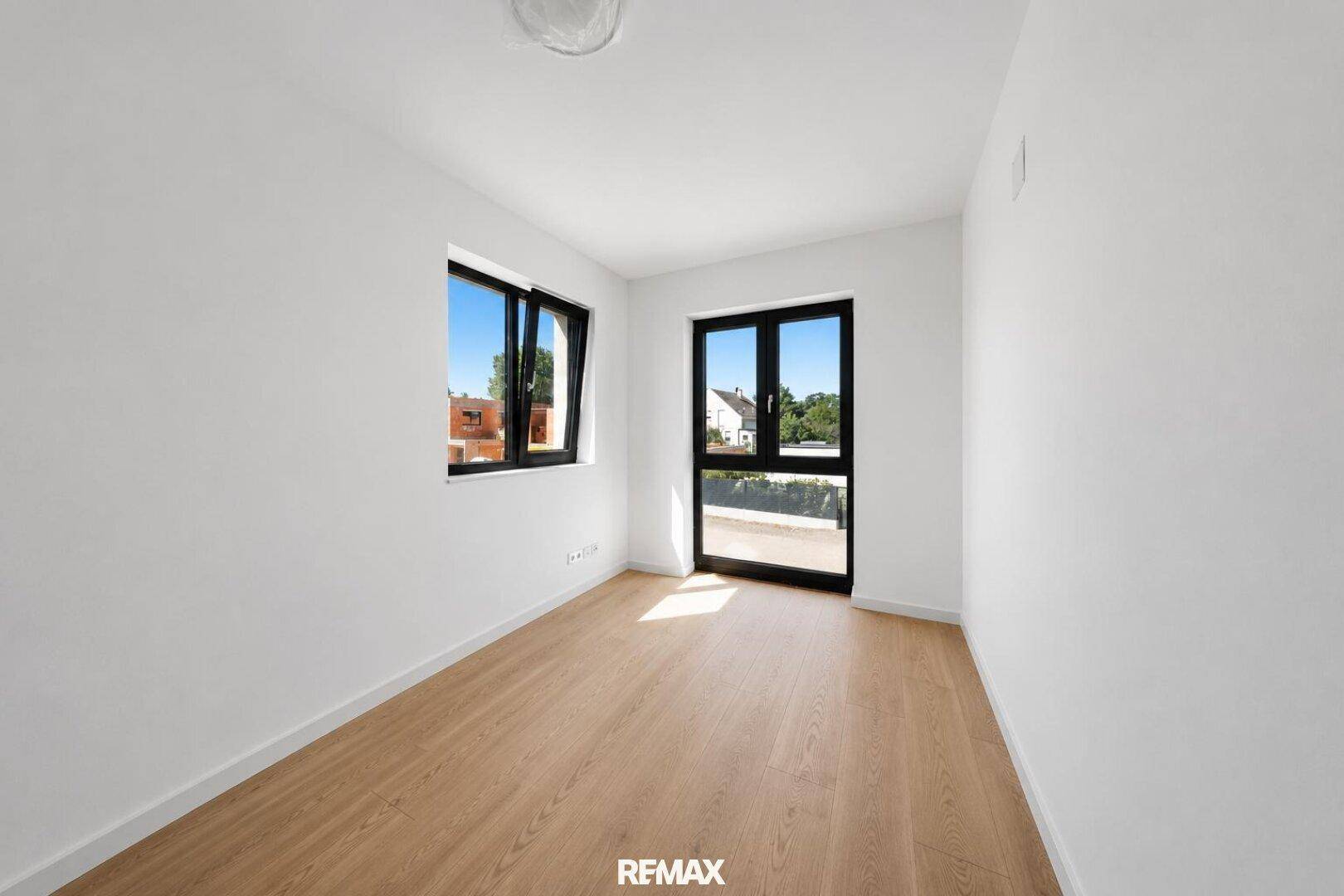 Helles, unmöbliertes Zimmer mit Holzboden, Fenster und Zugang zu einem französischen Balkon.