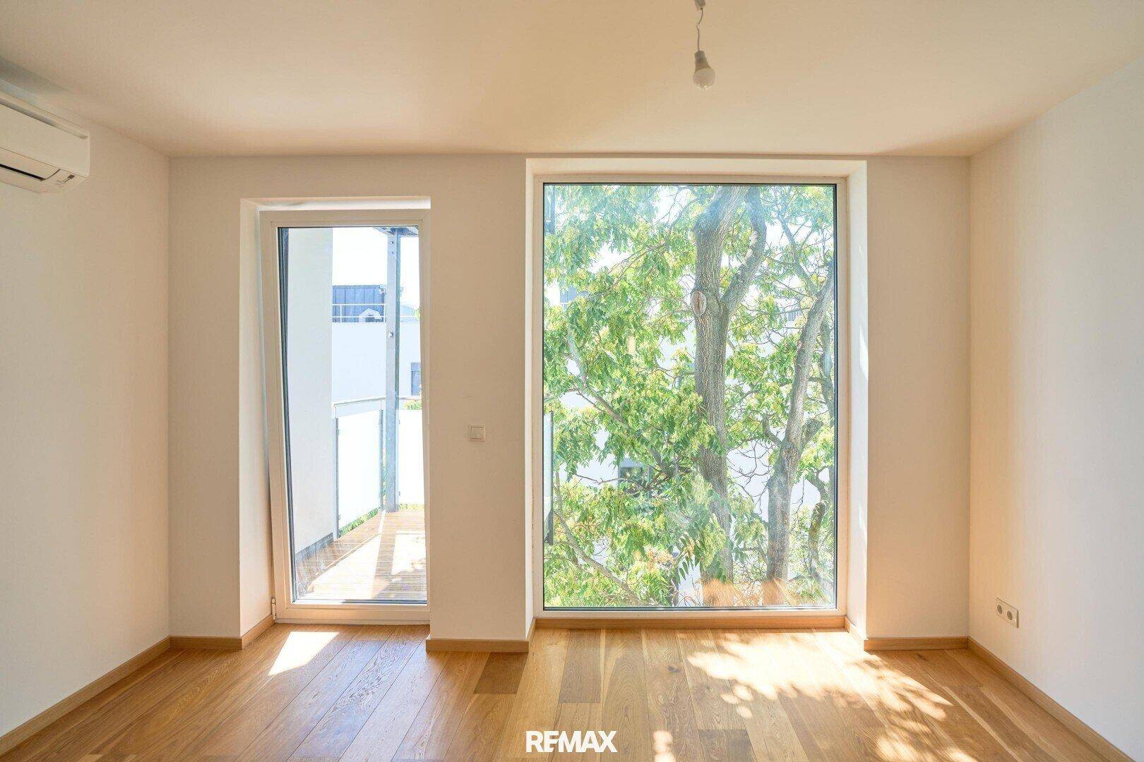 Heller Raum mit großem Fenster, Balkonzugang und schönem Blick ins Grüne.