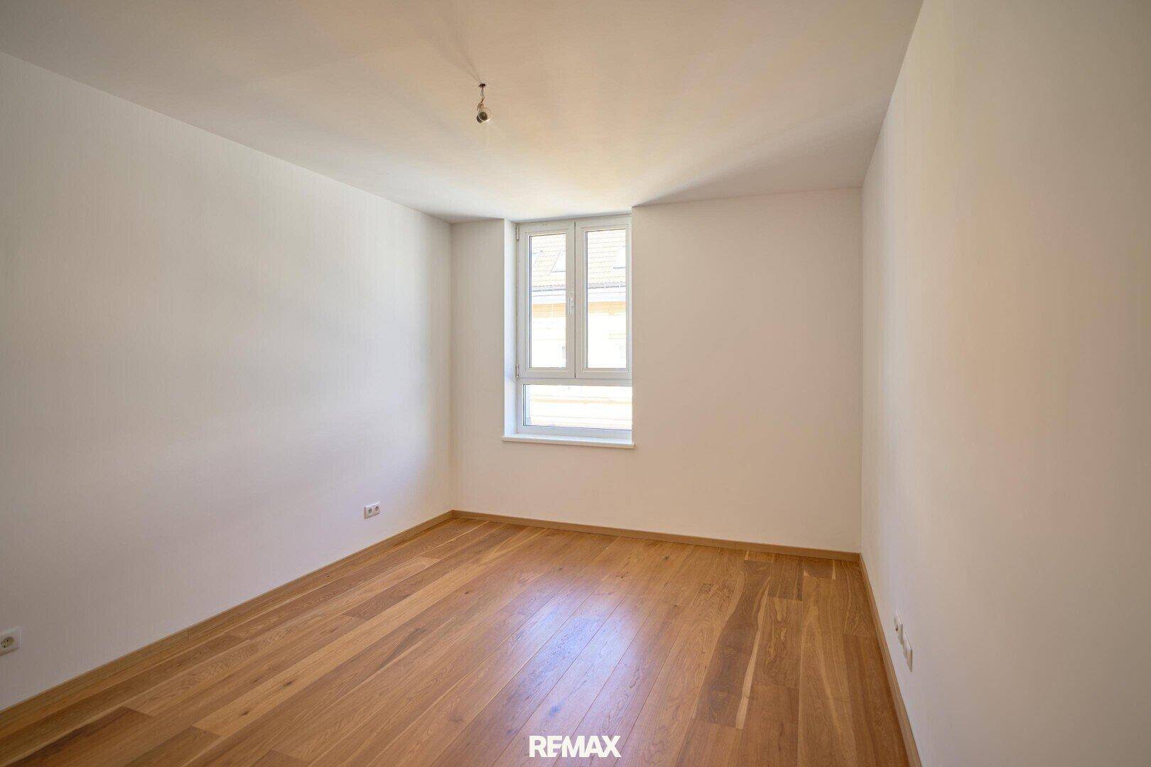 Helles Zimmer mit Parkettboden und einem Fenster, bereit zur individuellen Gestaltung.