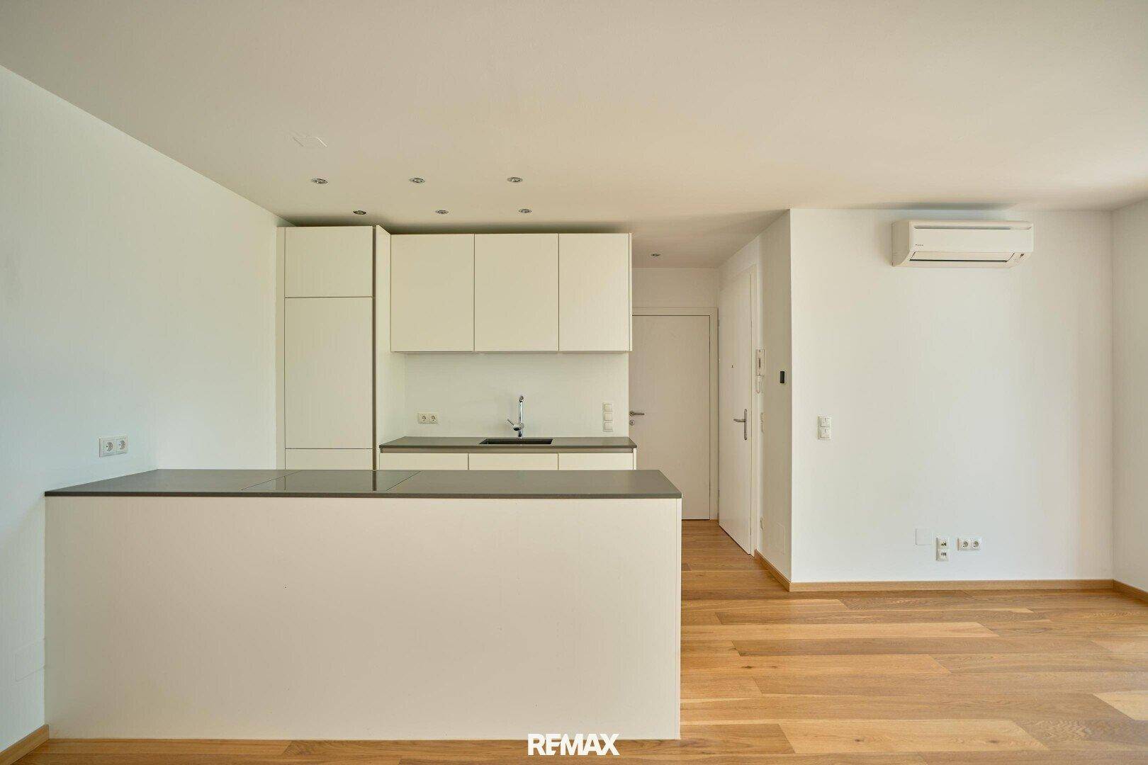 Moderne Einbauküche mit weißen Schränken, dunkler Arbeitsplatte und Parkettboden in offenem Design.