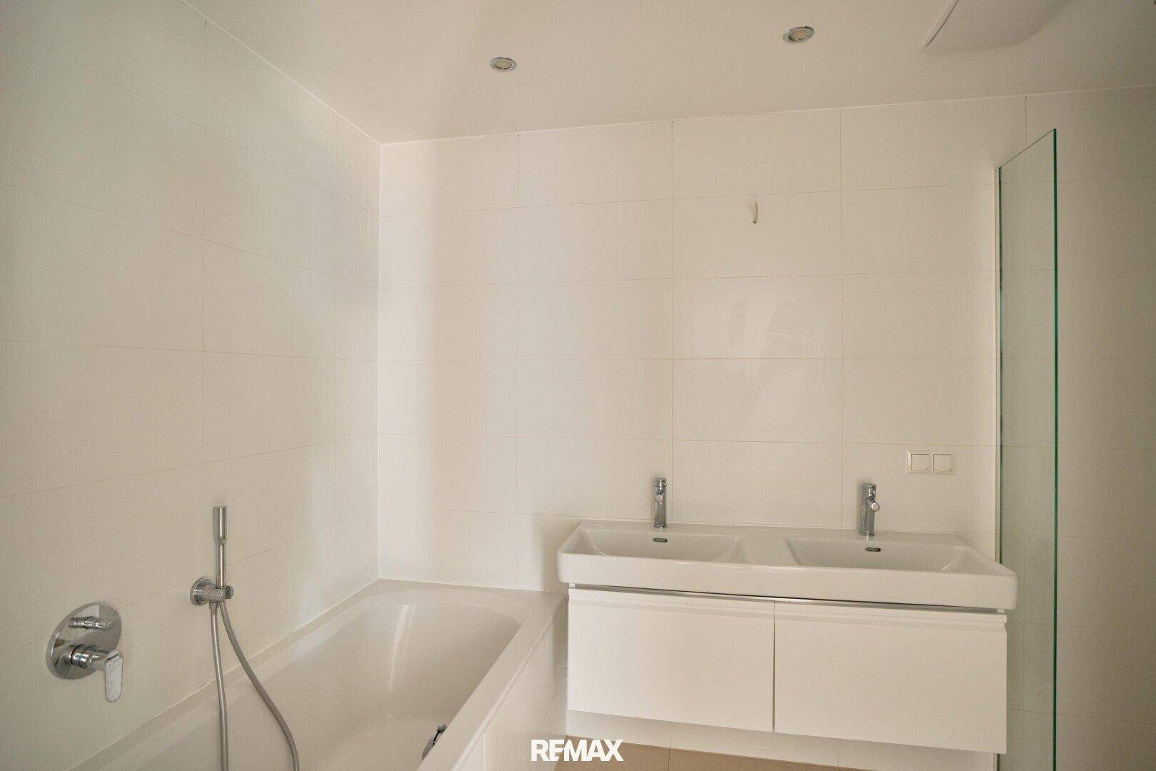 Modernes Badezimmer mit weißen Fliesen, Badewanne und Doppelwaschbecken.