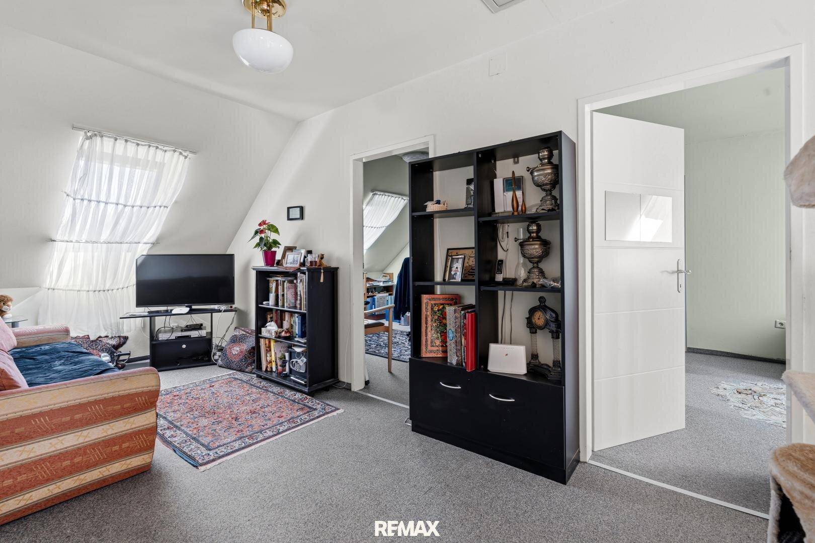 Gemütlicher Dachbodenraum mit schrägen Decken, Teppichboden und Bücherregalen, ideal als Rückzugsort.