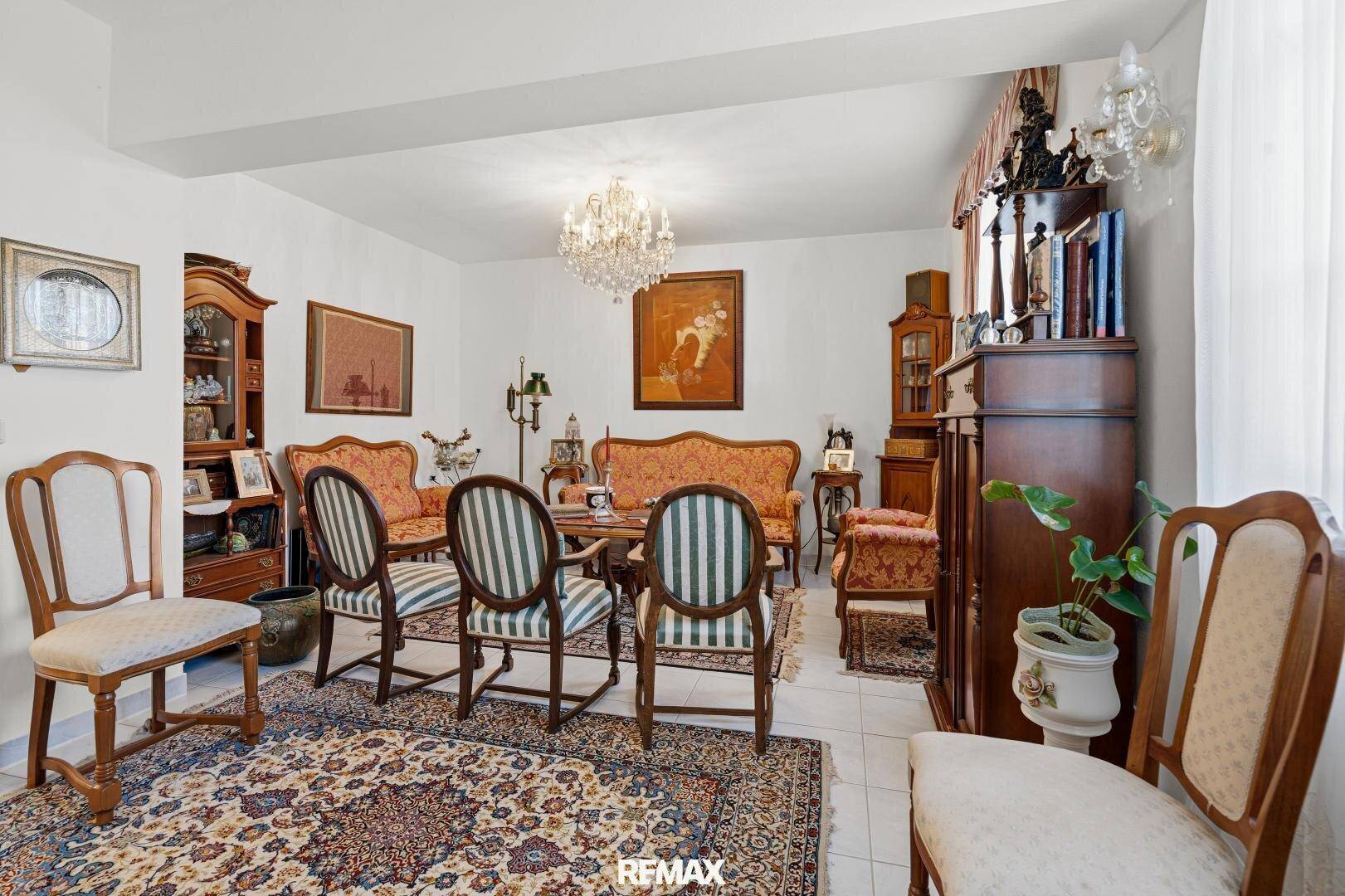 Geräumiges Wohnzimmer mit traditionellen Möbeln, einem Kronleuchter und einem gemusterten Teppich.