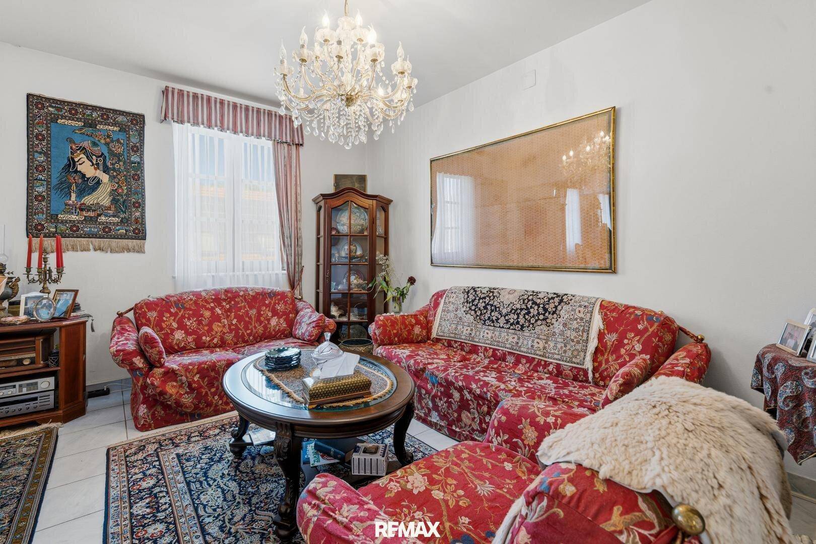 Traditionelles Wohnzimmer mit roten Blumensofas, einem Couchtisch und einem eleganten Kronleuchter.