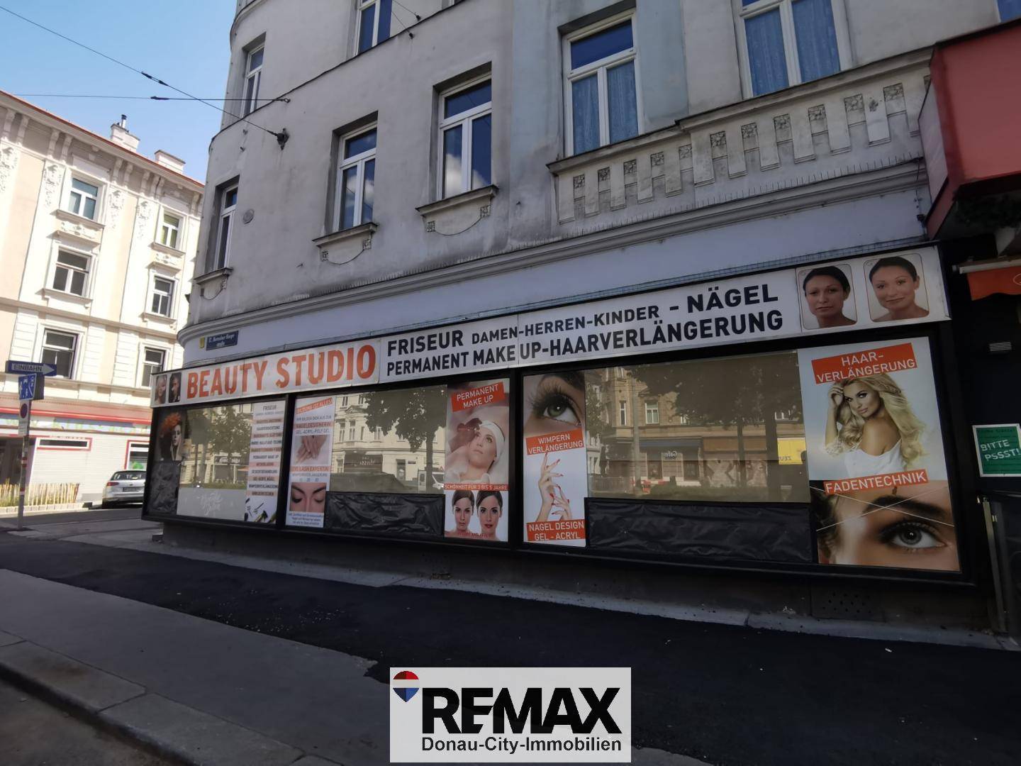 Seitenansicht eines Gebäudes mit Schaufenstern des "Beauty Studios" und Passanten auf dem Gehweg.