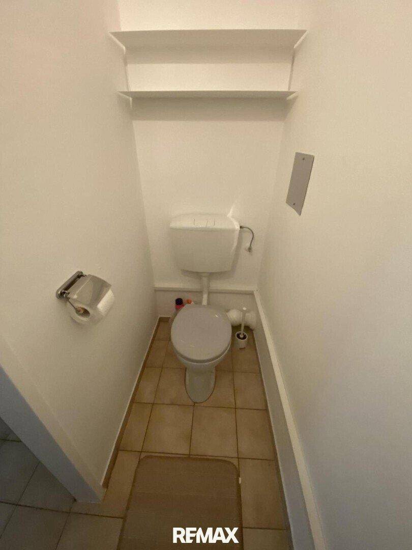 Separates WC mit Toilette, Fliesenboden und weißen Wänden, ausgestattet mit Ablageflächen.