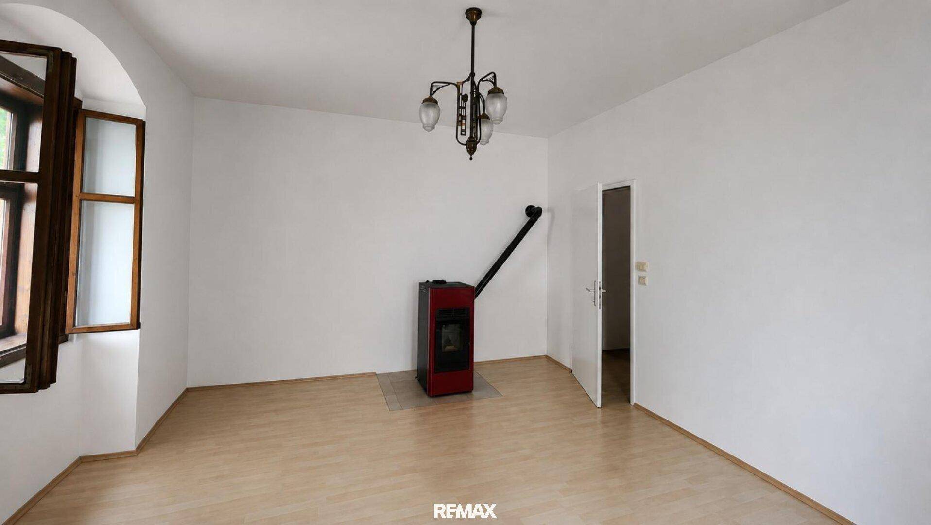 Geräumiges Zimmer mit Laminatboden, weißen Wänden und einem modernen roten Holzofen als Heizquelle.
