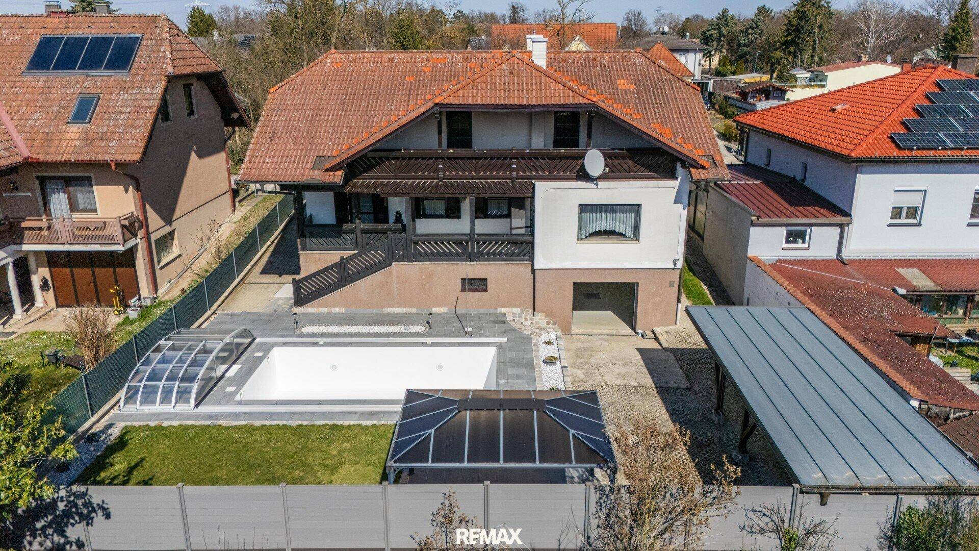 Luftaufnahme des Anwesens mit Haus, Poolbereich und umliegenden Gärten unter blauem Himmel.