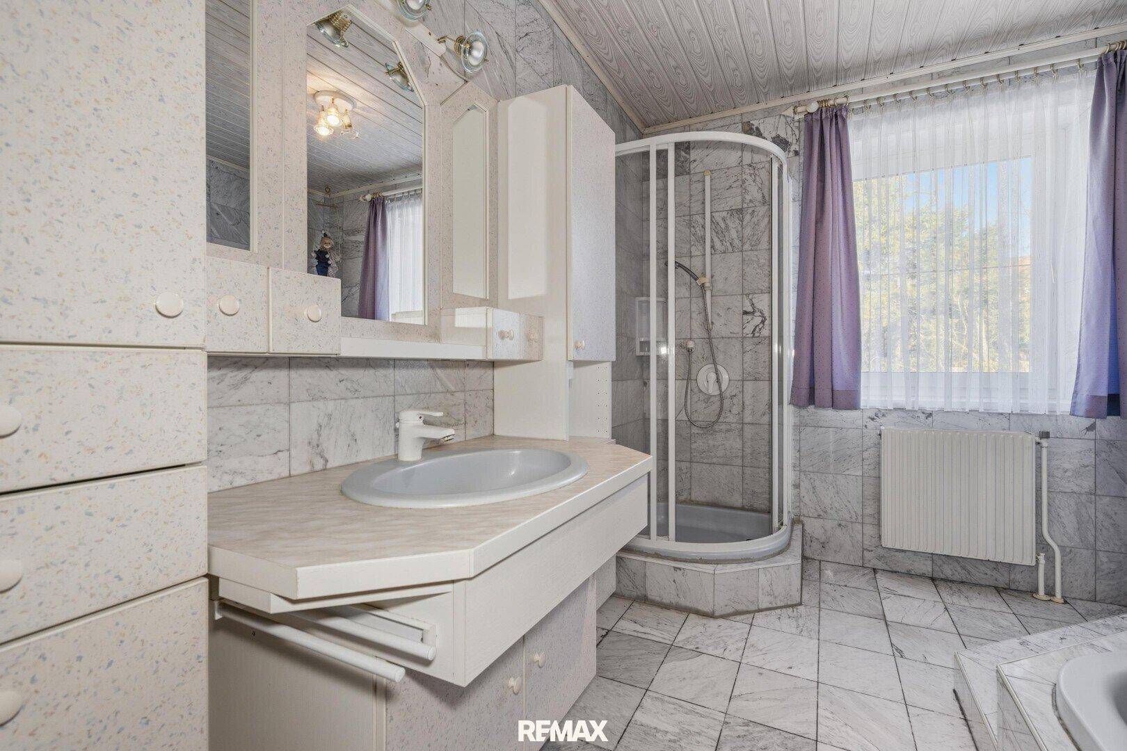 Badezimmer im 80er-Jahre-Stil mit gemusterten Fliesen, Duschkabine und Fenster.