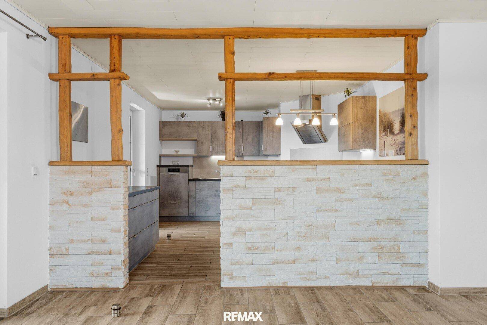 Halboffene Küche mit modernen grauen Schränken und Holzelementen, verbunden mit einem Wohnbereich.