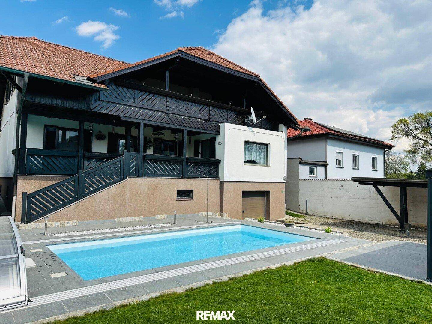 Ansicht des Hauses von der Gartenseite mit großem Pool und gepflegter Rasenfläche unter blauem Himmel.