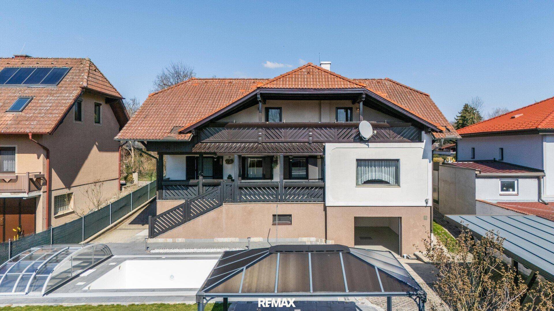 Vorderansicht des Hauses mit Satteldach, Balkon und Garage, umgeben von Grünflächen.