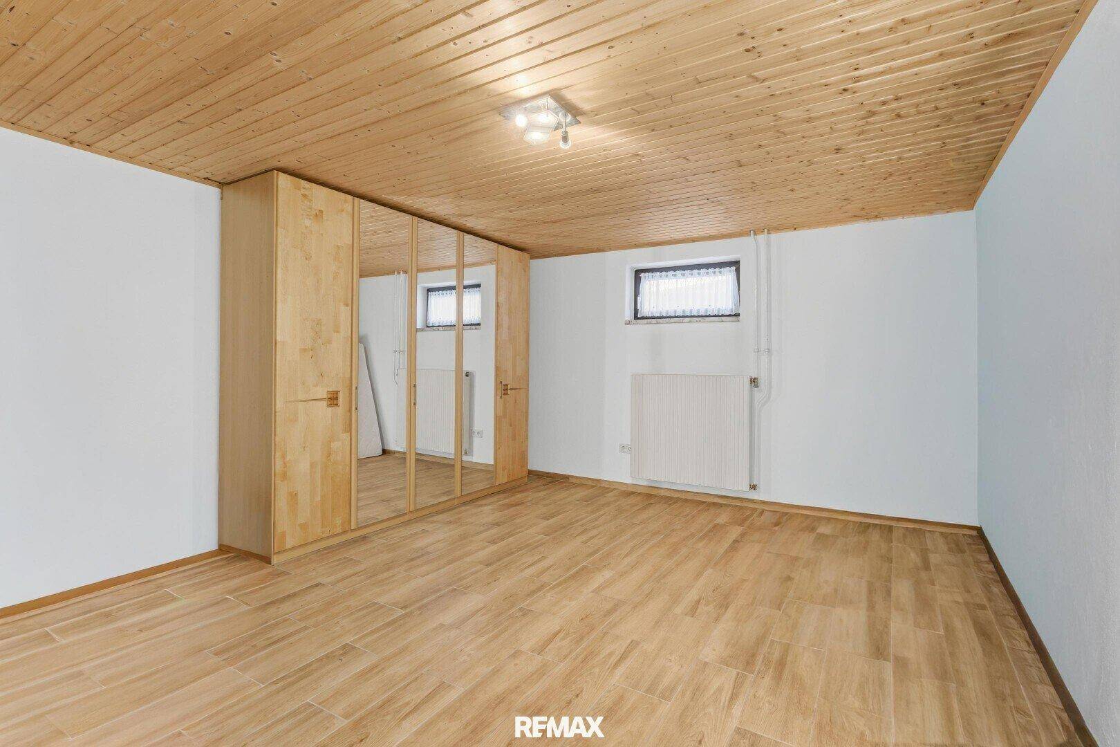 Geräumiges Schlafzimmer mit Laminatboden, Holzdecke und großem Spiegelschrank.