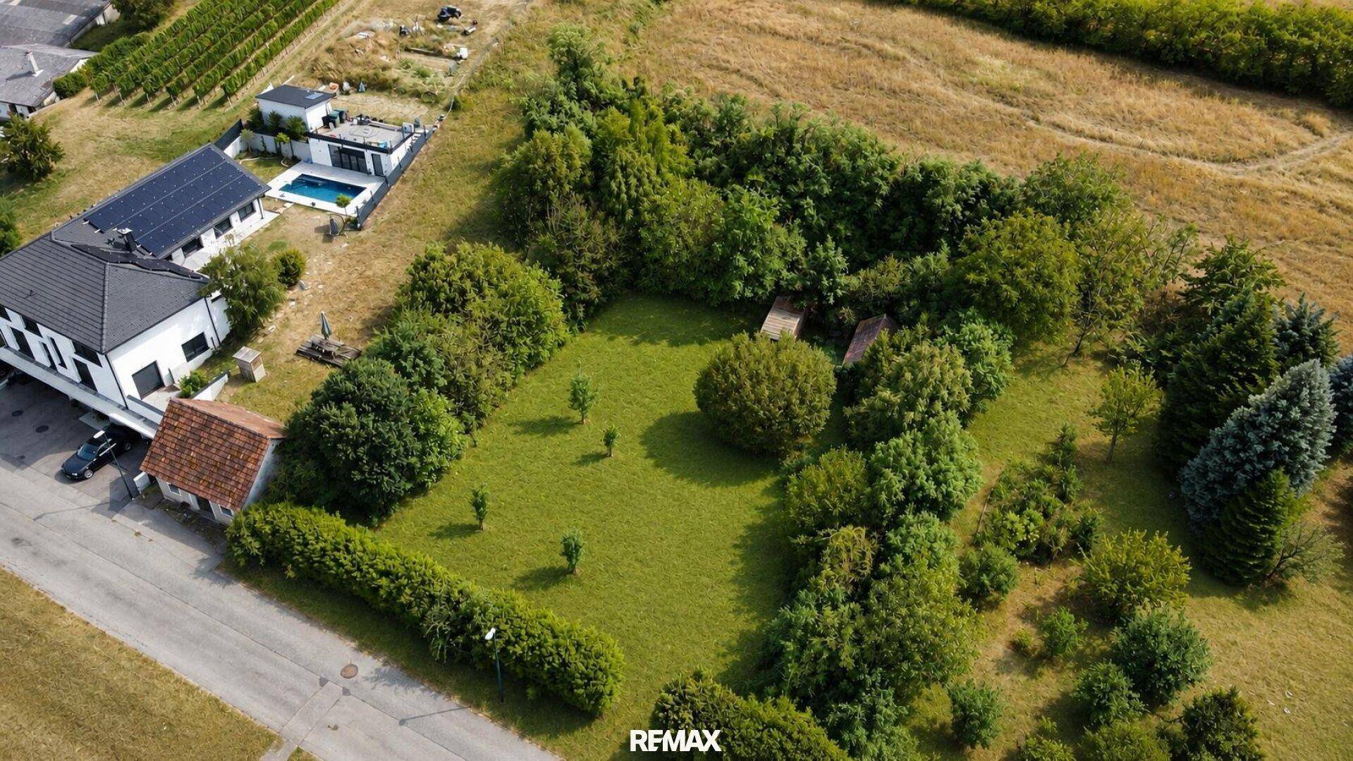 Luftaufnahme eines grünen Grundstücks umgeben von Häusern, Feldern und Weinbergen.