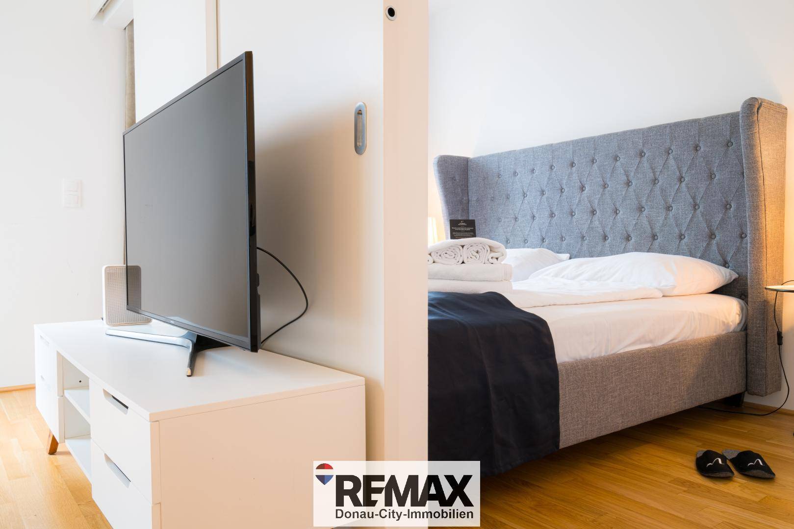 Schlafbereich mit großem Bett und Fernseher, durch eine Trennwand vom Wohnbereich abgetrennt.