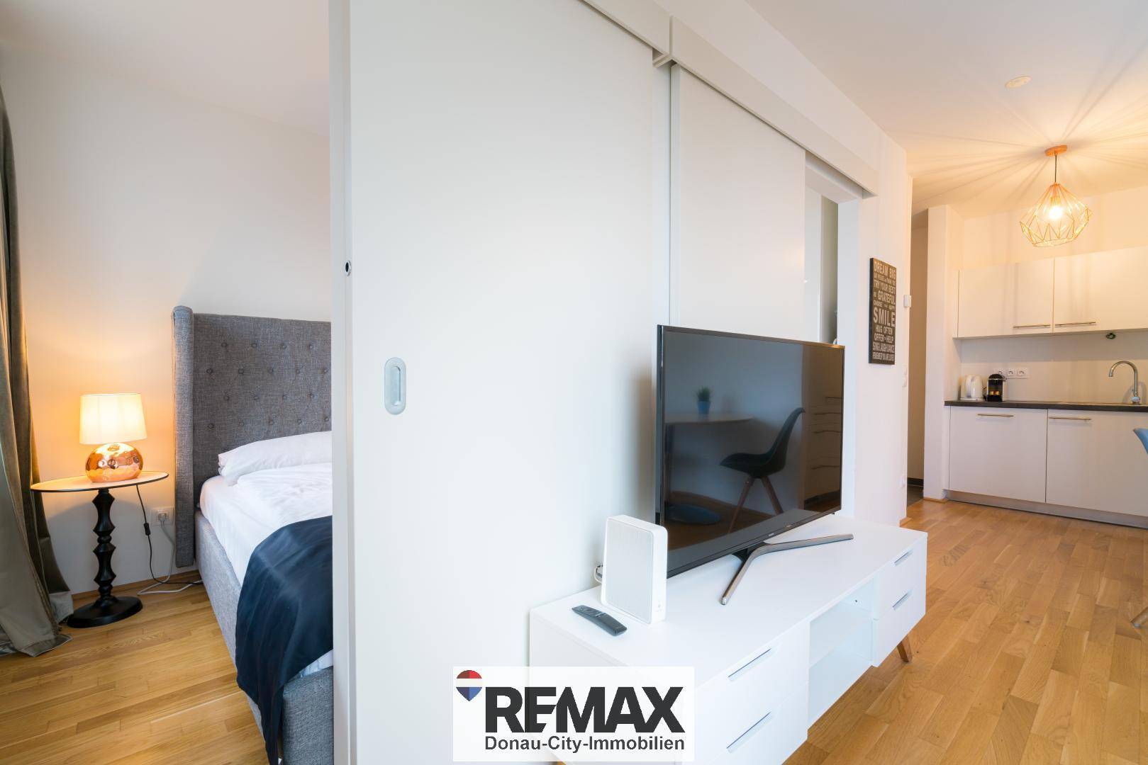 Schlafbereich mit Fernseher und Bett, offen zur Küchenzeile und dem Wohnbereich.
