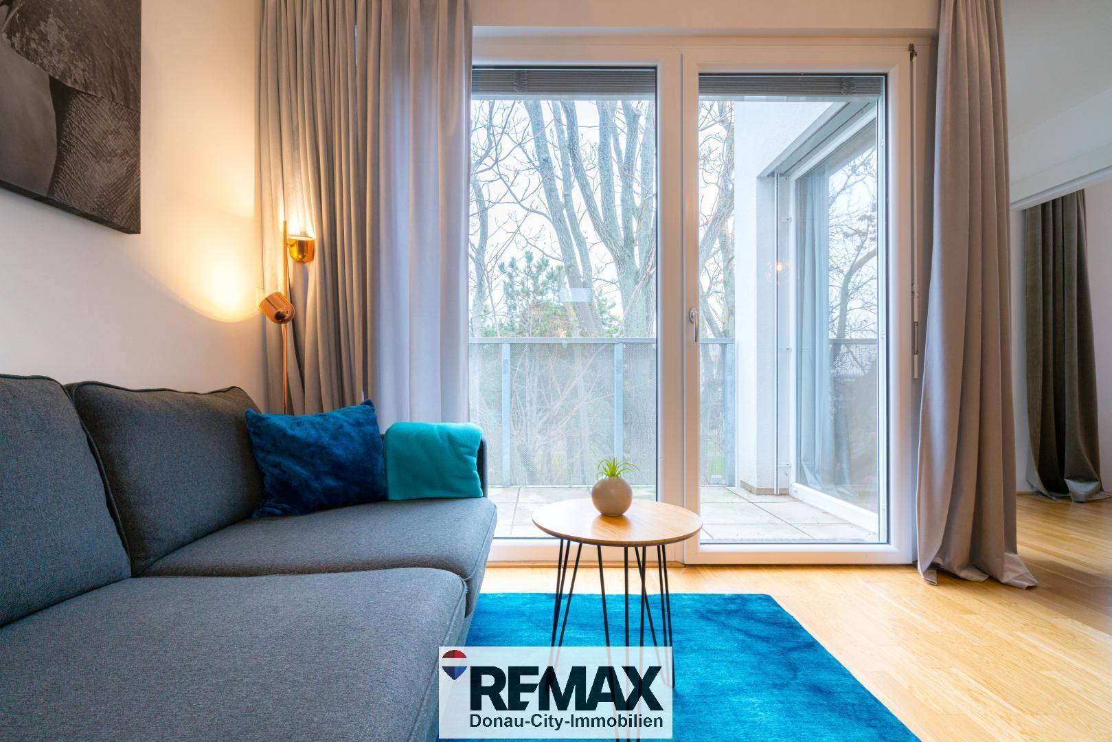 Gemütlicher Wohnbereich mit Sofa und direktem Zugang zu einer Außenterrasse durch große Fenster.