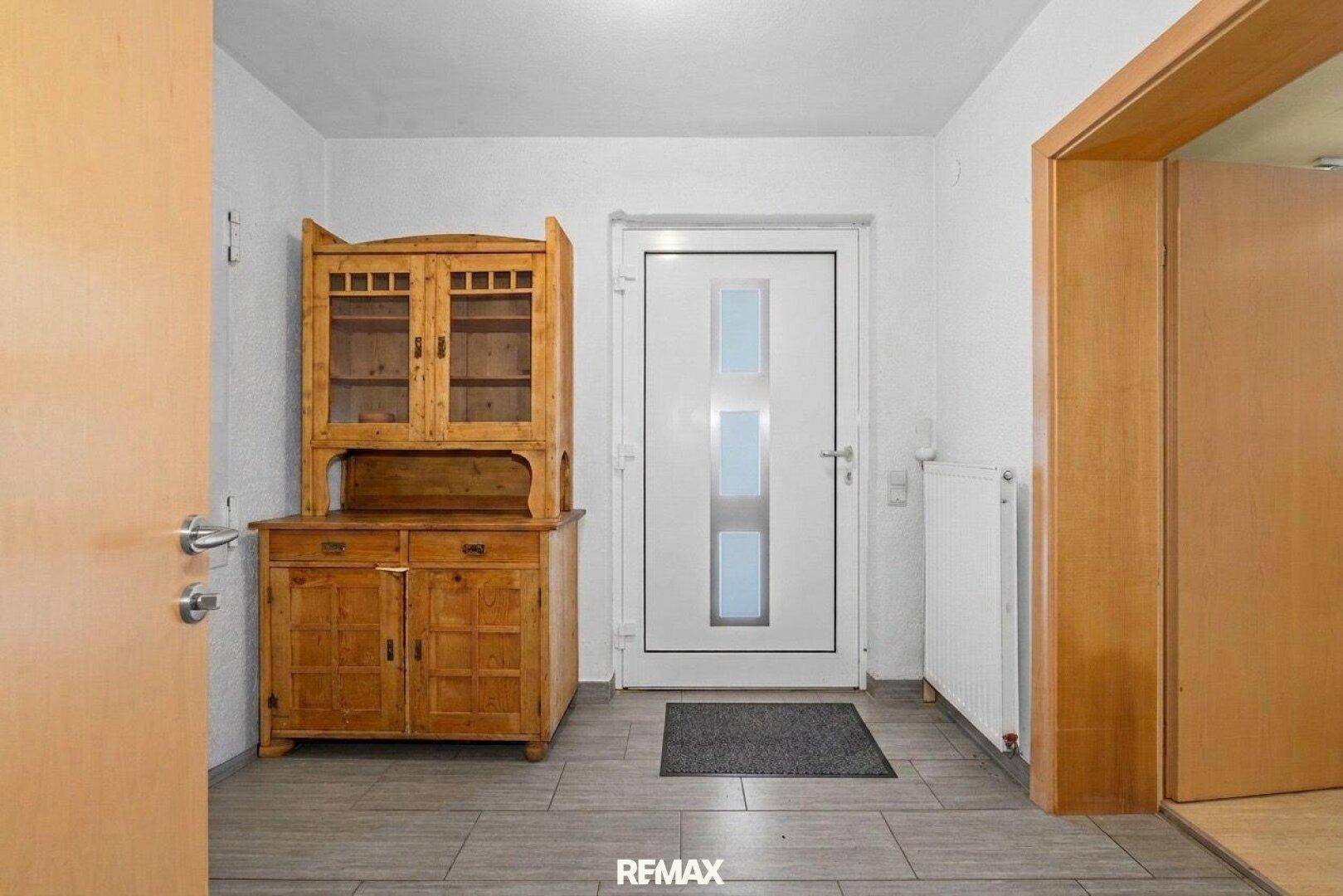Eingangsbereich mit Fliesenboden, weißer Tür und traditionellem Holzschrank.