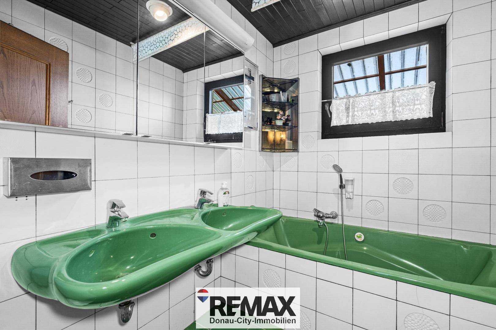 Badezimmer im 80er-Jahre-Stil mit grüner Badewanne, Doppelwaschbecken und weißen Fliesen.