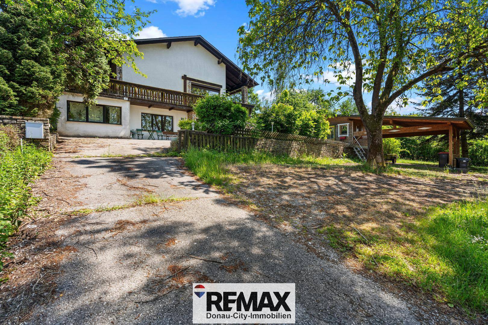 Zufahrt zum Haus mit Carport und viel Grün in einer ruhigen, ländlichen Umgebung.
