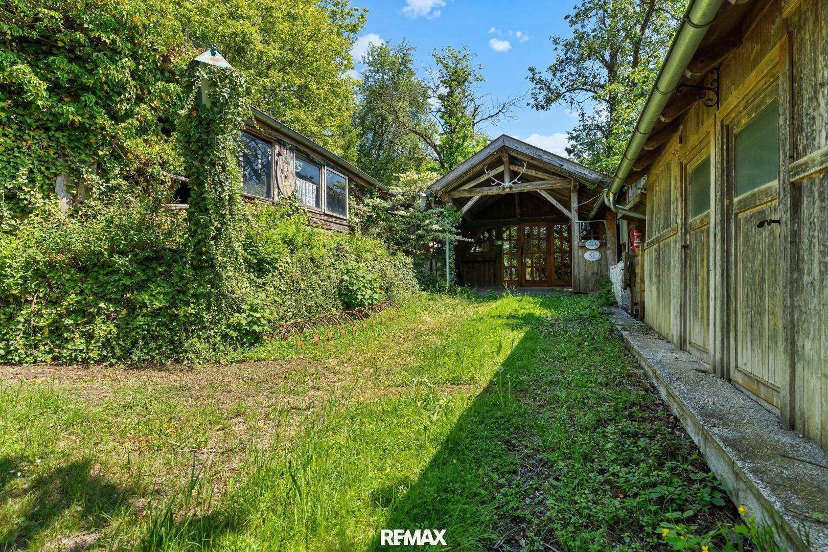 Naturbelassener Gartenbereich mit Holzhütten und üppiger Vegetation.