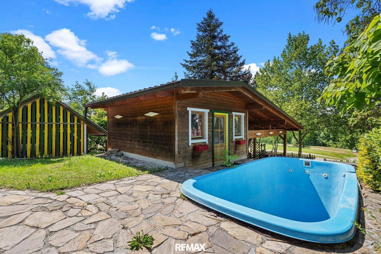Holzhaus mit kleinem Pool und gepflastertem Bereich im grünen Garten.