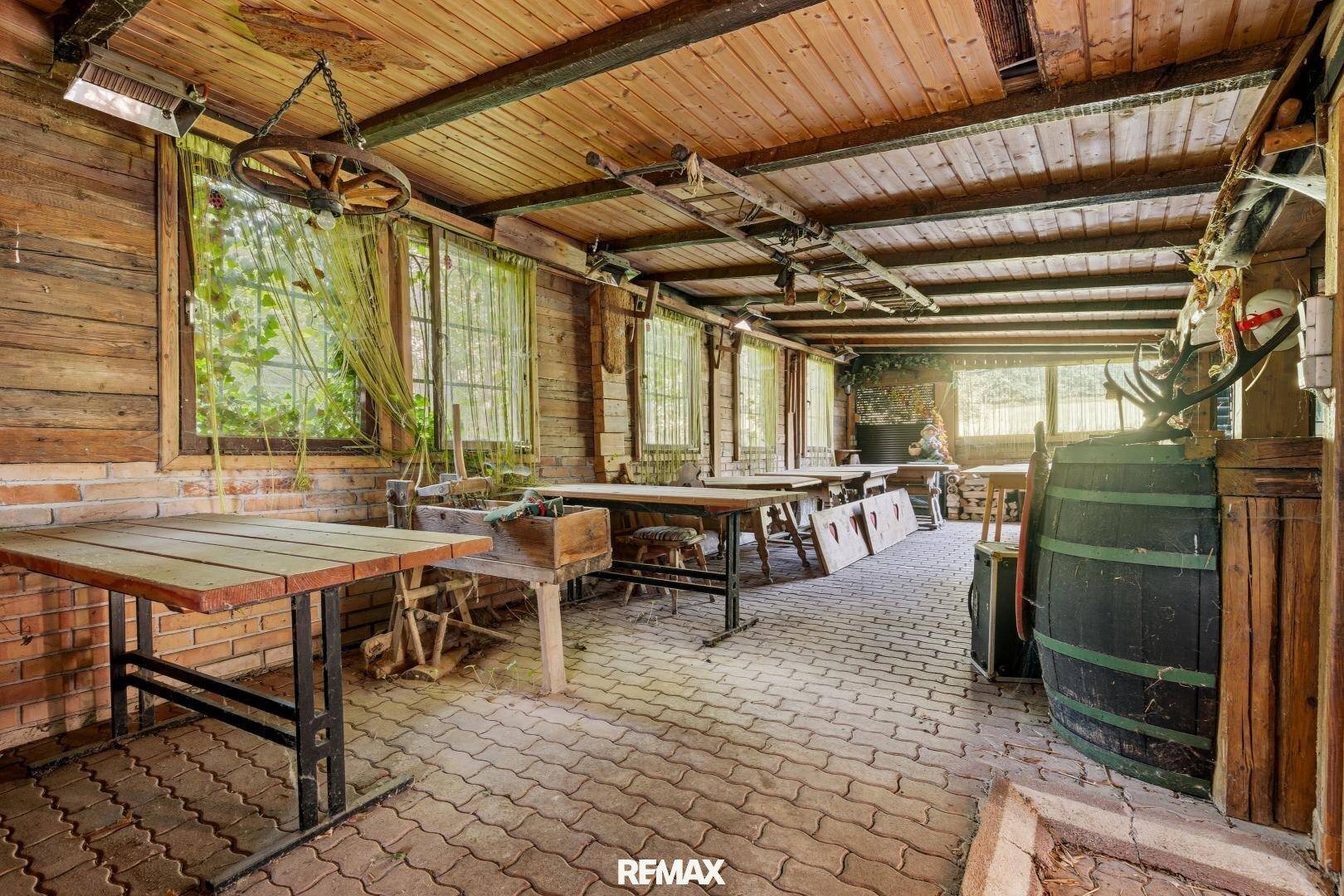 Großer rustikaler Raum mit Holzwänden, Holzbalkendecke und mehreren Holztischen, ideal für Versammlungen.